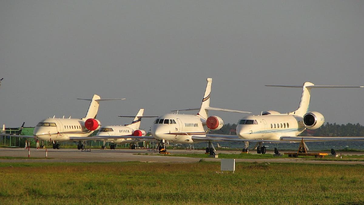 Four large business jets parked side by side on an airport apron.
