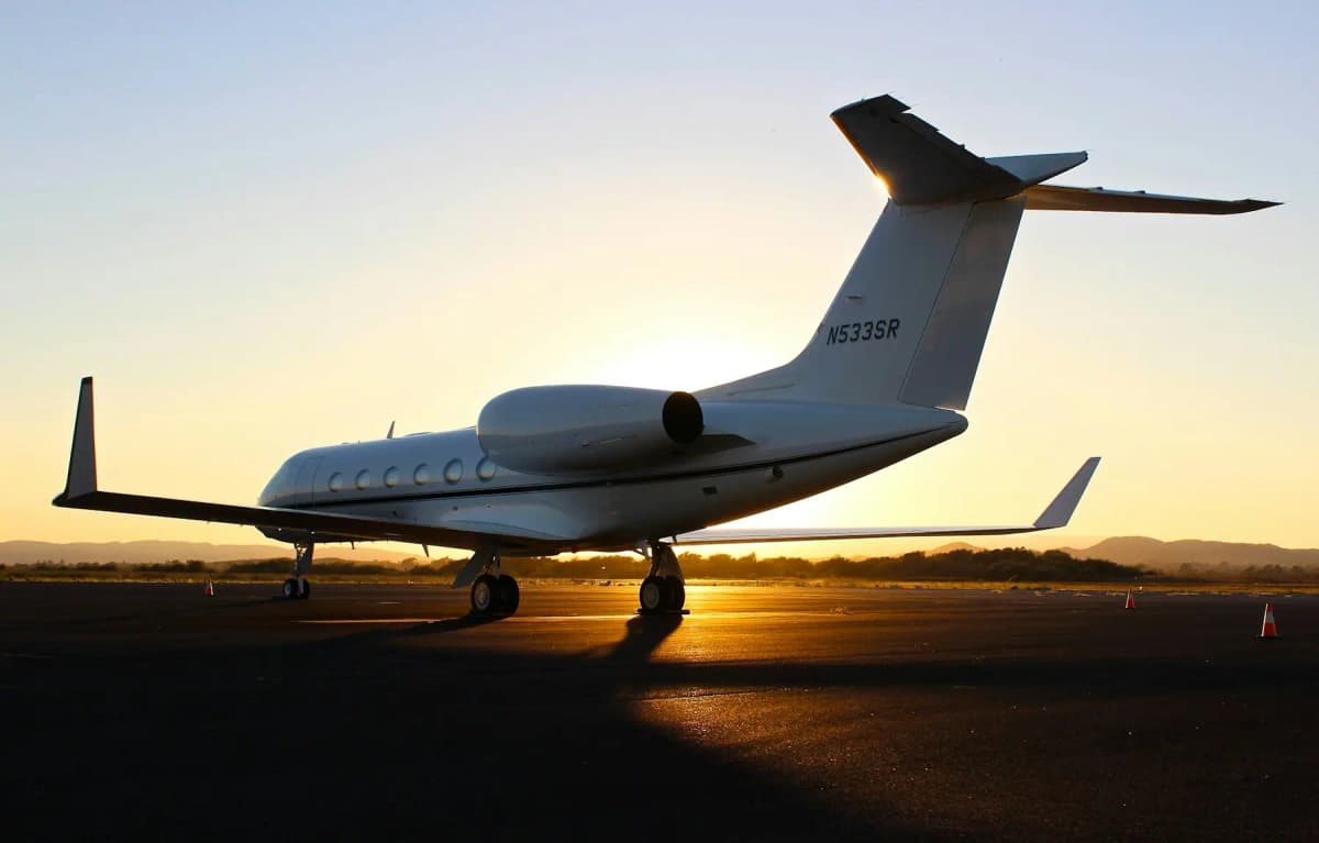 A Gulfstream business jet parked on an airport ramp at sunset, seen from behind.