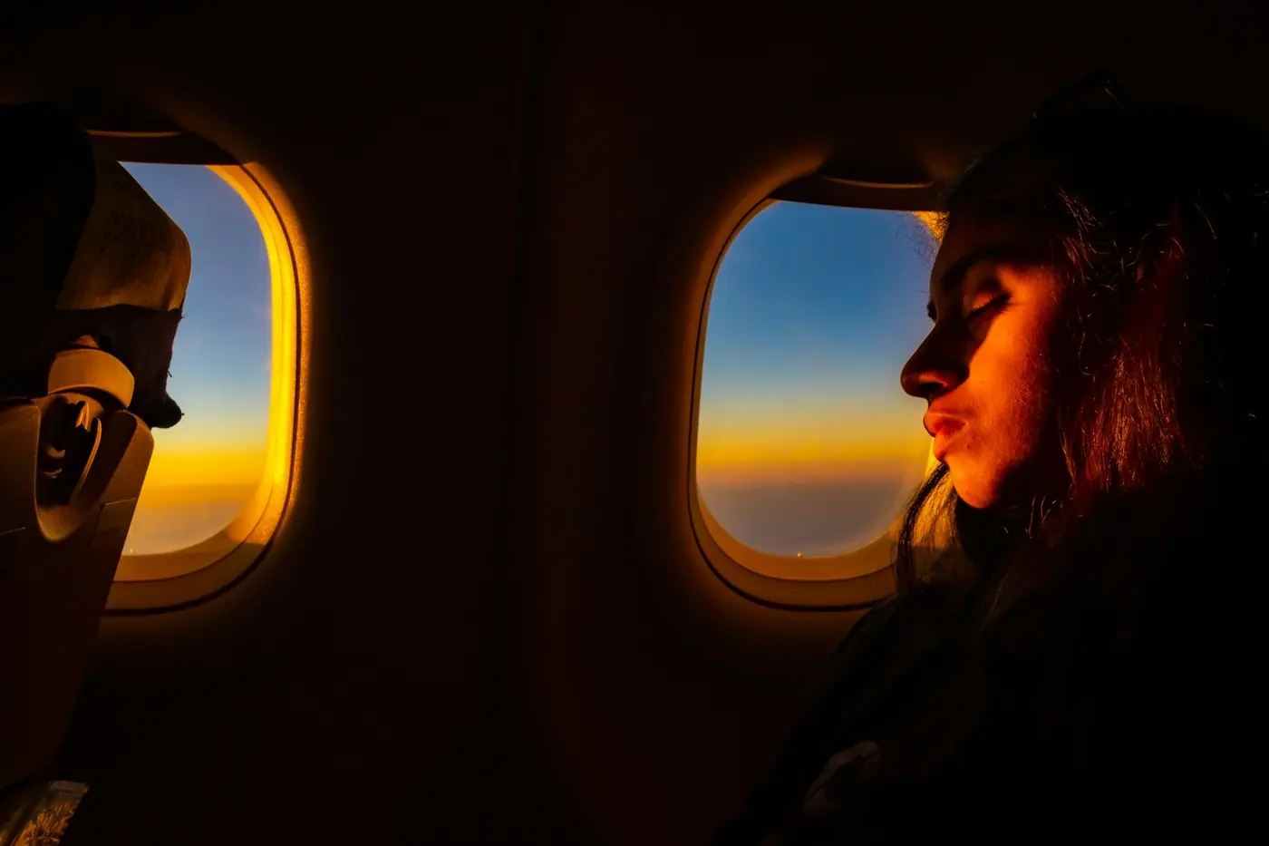 A passenger at an aircraft window at sunset, the horizon orange below a blue sky.